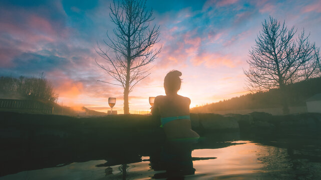Beautiful caucasian woman tourist enjoy sunset drink sparkling wine in famous secret lagoon, Iceland. Wellness and well-being recreational activities in Iceland