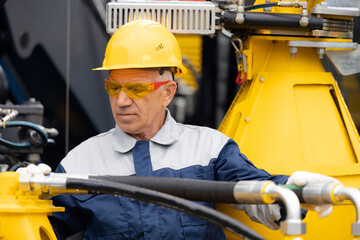 Adult man worker checks piping system of hydraulic hose valves in industrial equipment
