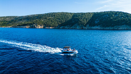 Obraz premium An aerial shot captured by a drone showing a boat cruising through the crystal-clear blue waters near the island of Cres. The scenic coastline, dotted with lush greenery and rocky cliffs