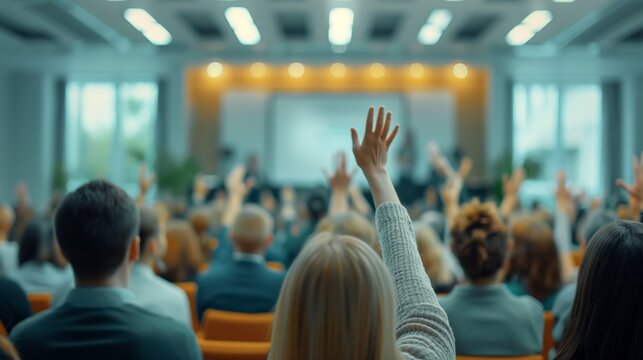 Audience members raising hands during a seminar or conference, implying active participation and engagement in a modern, well-lit venue.