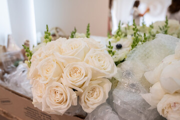 Bridal bouquet of white roses lying in front of mirror with bride reflected in background while getting ready