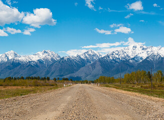 Fototapeta premium A winding gravel road leading toward snow-capped mountains