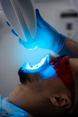 Patient whitens his teeth wearing goggles and lip retractor. Dental whitening procedure by...