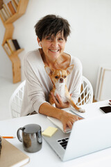 Smiling freelancer holding small dog and using laptop at home