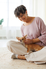 Obraz premium Happy mature woman petting Chihuahua dog on carpet at home