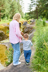 Fototapeta premium Childhood concept. Mom and boy walk hand in hand along a path in the forest