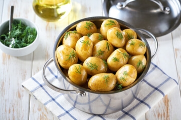 Boiled young potatoes with butter and fresh dill in a white wooden table, selective focus. Top view.