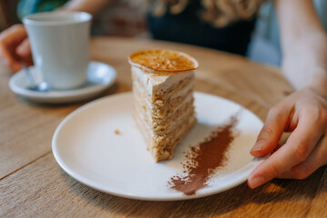 Close-up of slice of layered cake with cup of coffee on wooden cafe table, capturing a cozy and inviting moment.