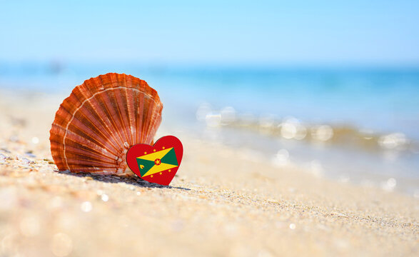 Sandy beach in Grenada. Flag of the Grenada in the shape of a heart and a large shell.