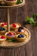 Berry tartlets with butter cream lie on a wooden whatnot outdoors on the table