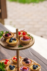 Berry tartlets with butter cream lie on a wooden whatnot outdoors on the table
