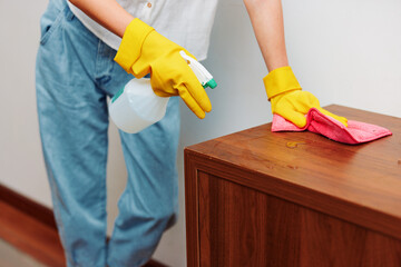 Cleaning concept woman in blue jeans and yellow rubber gloves cleans furniture with spray bottle and rag
