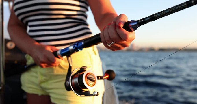 Woman with rod fishes standing on sailing motorboat at summer sunset slow motion. Lady catches fish during sea journey. Active hobby and lifestyle