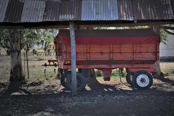 Obraz premium rural scene with a red grain cart parked beneath an old corrugated metal shed