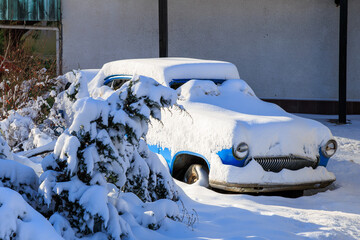A blue car is covered in snow and is parked in a driveway, winter background or backdrop