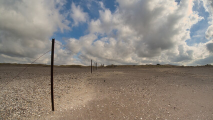 Fototapeta premium old and weathered wire fence stretching across a sandy beach, which appears to be devoid of people limiting access to certain areas of the beach