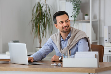 Fototapeta premium Handsome businessman working with laptop at table in office