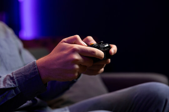 Close up shot of gamepad controller in man hands playing intense online videogame in neon illuminated living room. Gamer participating in internet esports competition, playing on gaming console