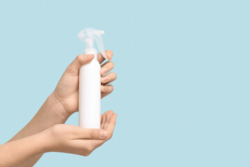 Female hands with bottle of cosmetic spray on blue background