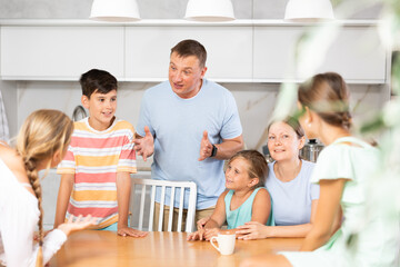 Friendly family gathered at table and cheerfully discuss past day. Mom, dad, three daughters and son solve important issue in friendly atmosphere