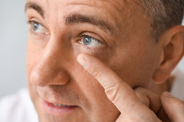 Mature man putting in contact lenses on grey background, closeup