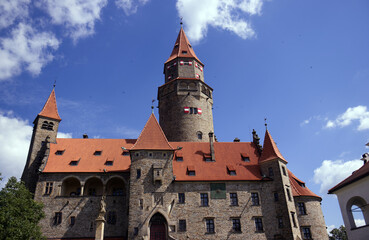 Old stone castle with tower and red roof. Historic building, Middle Ages, stone castle. Blue sky with white clouds above the castle. Tourist place, sights, travel, holidays