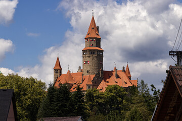 an old stone castle with a red roof and round towers. A castle on a wooded hill. Nature, landscape, castle. Medieval. Blue sky with clouds above the castle.