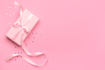 Gift box tied up with pink ribbon and confetti on pink background. Top view