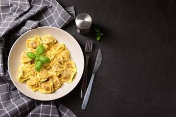 Plate of boiled dumplings with cheese and basil on black background