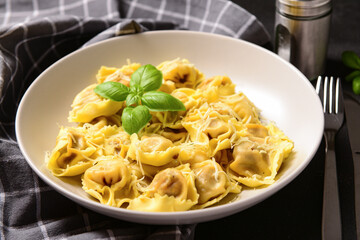 Plate of boiled dumplings with cheese and basil on black background