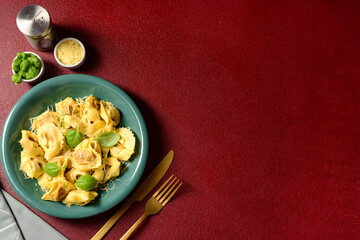 Bowl of boiled dumplings with cheese and basil on red background