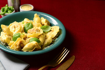 Bowl of boiled dumplings with cheese and basil on red background