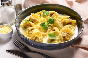 Bowl of boiled dumplings with sauce and basil on white background