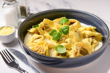 Bowl of boiled dumplings with sauce and basil on white background
