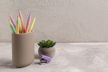 Holder with pens, stapler and flowerpot on light background