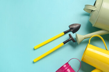 Watering cans with gardening rake and shovel on blue background