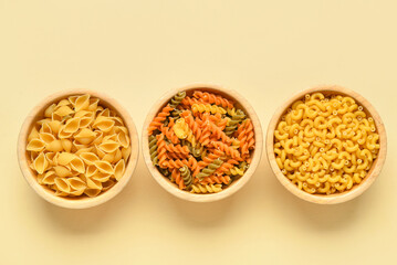Bowls with different tasty uncooked pasta on beige background