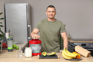 Sporty muscular man with protein powder and food on table in kitchen