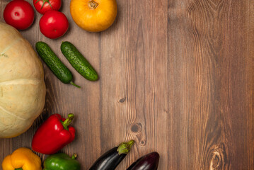 Pumpkins, eggplants, cucumbers, tomatoes and peppers of different colors on wooden background. Autumn harvest. Copy space, top view