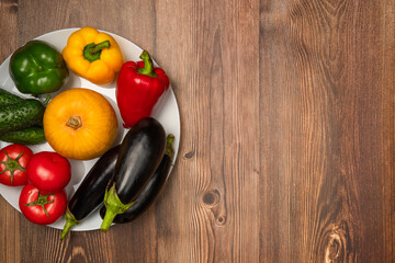 Pumpkins, eggplants, cucumbers, tomatoes and peppers of different colors on the plate. Autumn harvest. Copy space, top view