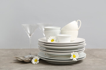 Beautiful tableware and chamomiles on table near grey wall