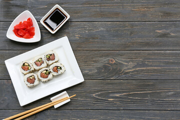 Tasty sushi rolls with soy sauce, chopsticks and marinated ginger on wooden background