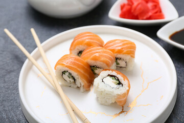 Plate with tasty sushi rolls and chopsticks on black grunge background, closeup