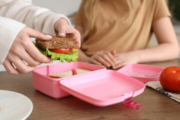 Mother with daughter packing food into school lunchbox in kitchen, closeup