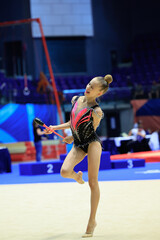 A young rhythmic gymnast performs a ribbon routine in a competitive setting, capturing focus and grace.