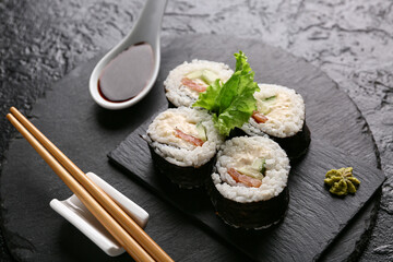 Tasty sushi rolls and chopsticks, spoon with soy sauce on black grunge background, closeup