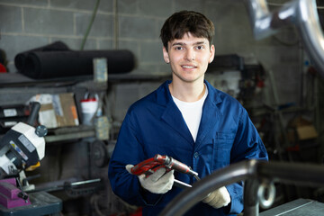 Young male worker in uniform posing with vice in metallurgical workshop