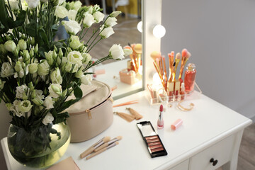 Decorative cosmetics and vase with flowers on table in dressing room