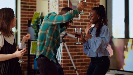 Asian, african american and caucasian group of friends dancing at apartment party, entertaining themselves, feeling the rhythm. Diverse colleagues doing energetic dance moves on bouncy music