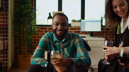 Portrait of African american man laughing with his friends, toasting with alcoholic drinks, celebrating special occasion in cozy apartment. Colleagues bonding together in stylish house